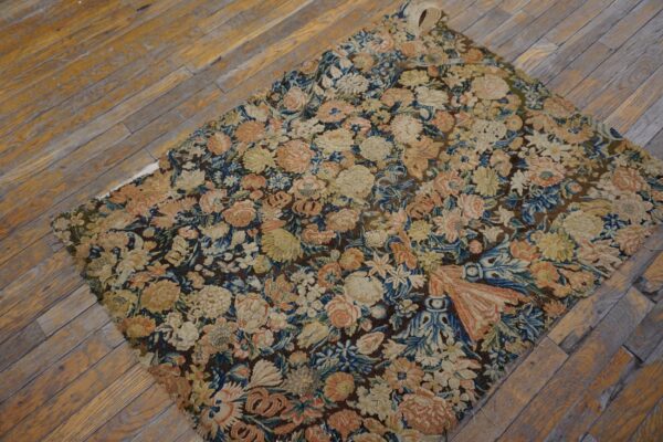 Muted floral tapestry rug with blue, peach, and beige colors shown on distressed wood planks.