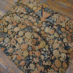 A dark, low-pile rug with dense floral patterns in cream, pink, and blue rests on distressed wood flooring.