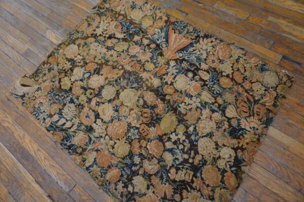 A dark, low-pile rug with dense floral patterns in cream, pink, and blue rests on distressed wood flooring.