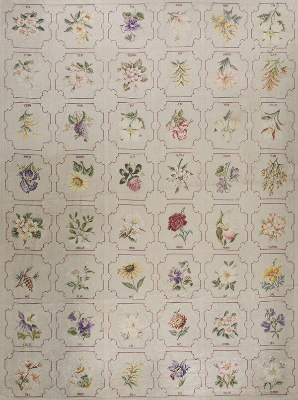 A light beige rug features a repeating grid pattern of colorful floral motifs and two-letter state abbreviations.