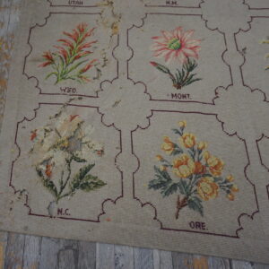 Worn beige low-pile rug with floral and lettered panels rests on heavily peeling gray wood floor.