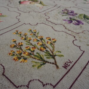 Low-pile beige rug with stitched multicolored florals and scalloped maroon borders defining the decorative squares.