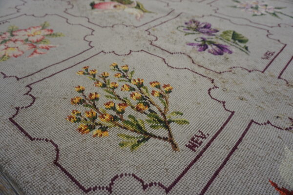 Low-pile beige rug with stitched multicolored florals and scalloped maroon borders defining the decorative squares.