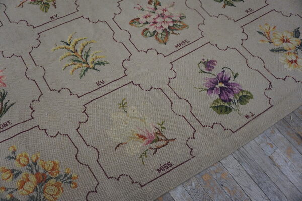 Beige low-pile rug featuring framed floral tapestry squares rests on distressed gray wood flooring.