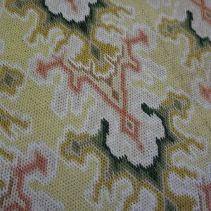 Detailed view of a tight-stitched rug with scrolling floral designs in yellow, cream, dark green, and coral.