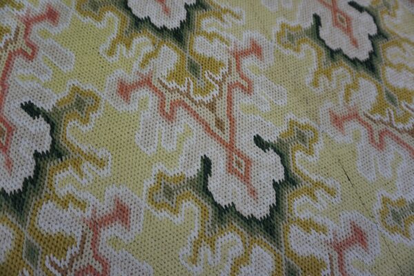 Detailed view of a tight-stitched rug with scrolling floral designs in yellow, cream, dark green, and coral.