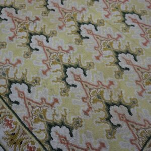 Low-pile rug with repeating patterns in pale yellow, white, green, and faded orange on wood flooring.