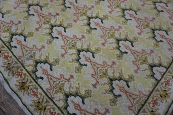 Low-pile rug with repeating patterns in pale yellow, white, green, and faded orange on wood flooring.