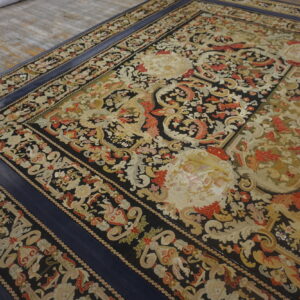 Black and gold classical patterned rug featuring red accents and a wide solid blue border, resting on wood.