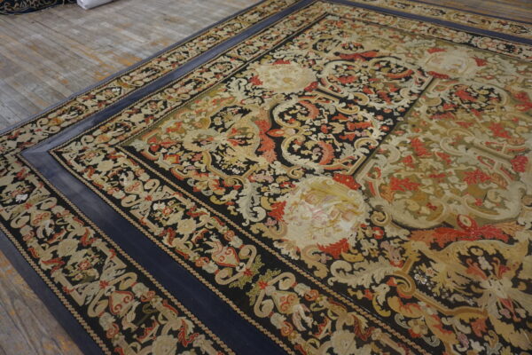Black and gold classical patterned rug featuring red accents and a wide solid blue border, resting on wood.
