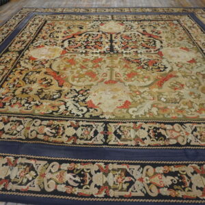 Low-pile rug with intricate scrolling patterns in navy, green, red, and cream on a wooden floor.