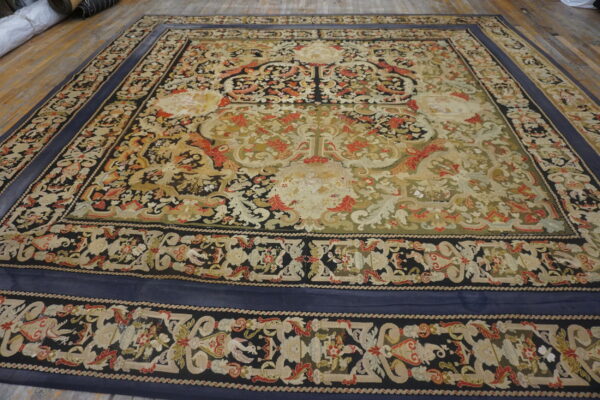 Low-pile rug with intricate scrolling patterns in navy, green, red, and cream on a wooden floor.