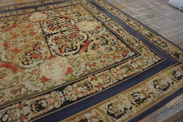 Ornate floral and scroll flatweave rug featuring black, olive, red, and tan colors, bordered in solid navy blue.