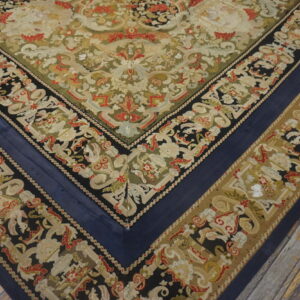 Corner of an ornate flatweave rug with deep blue, black, olive, and red patterns on weathered wood planks.