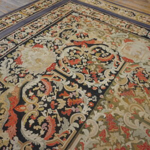 Ornate low-pile rug featuring black, cream, and red floral designs with a blue-gray border on wooden flooring.