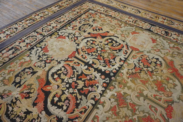 Ornate low-pile rug featuring black, cream, and red floral designs with a blue-gray border on wooden flooring.