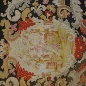 Low-pile needlepoint rug featuring dark ground, colorful baroque foliage, and a central cartouche scene.