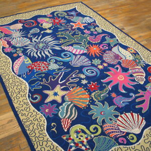 Low pile rug featuring a bright blue and pink marine pattern with a beige wavy border, lying on wood flooring.