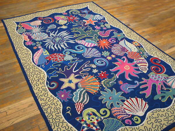 Low pile rug featuring a bright blue and pink marine pattern with a beige wavy border, lying on wood flooring.