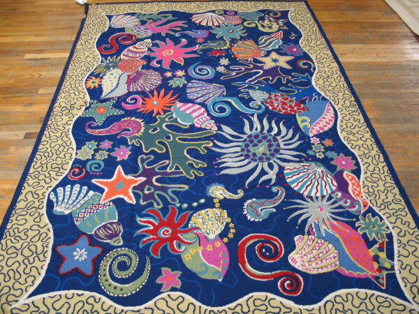 A large, low-pile blue rug features a vibrant, colorful undersea motif and a tan squiggly border on a wood floor.