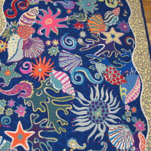 Multi-colored rug featuring whimsical sea life designs on blue, framed by a wavy beige border on wood floors.