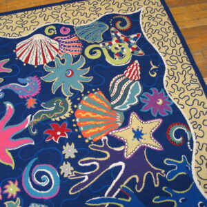 Colorful low-pile rug with abstract sea life on blue, bordered by tan wavy lines, on wood floor.
