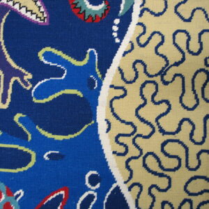 Low-pile abstract rug in blue, cream, red, and purple with a tight weave visible on a wood floor.