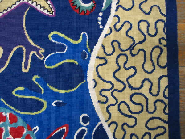 Low-pile abstract rug in blue, cream, red, and purple with a tight weave visible on a wood floor.