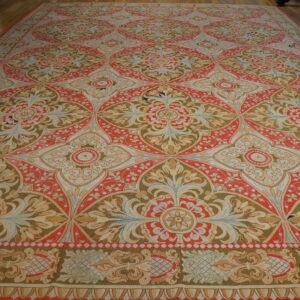 Large, low-pile rug with repeating coral, tan, and olive medallions covering a wooden floor.