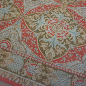 Flat-woven rug displaying large, detailed medallions in coral red, olive green, cream, and blue on a wood floor.