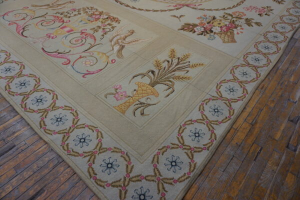 Low-pile beige rug with pink, blue, and yellow pastoral scenes and a repeating border on wood floors.