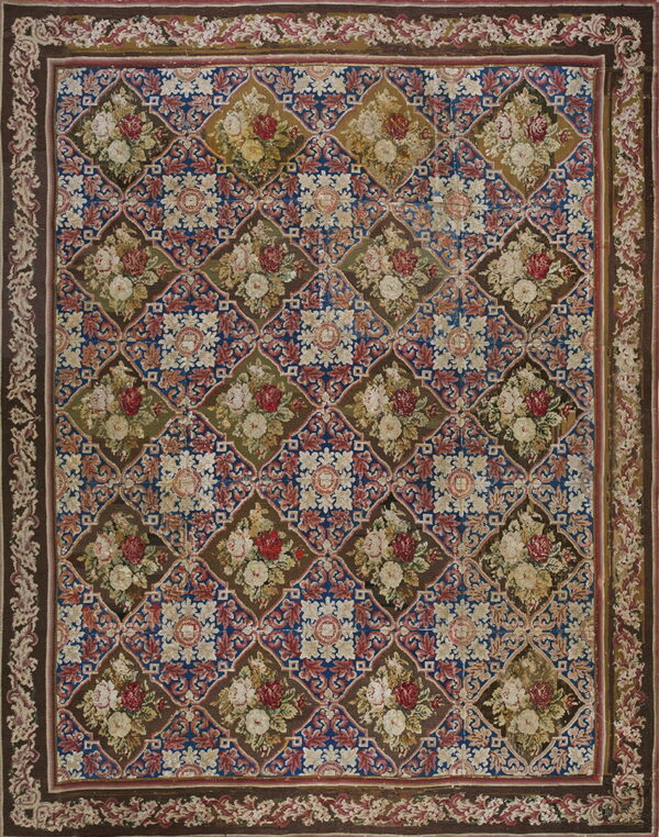 Ornate needlepoint-style rug featuring a brown, blue, and red diamond lattice filled with floral bouquets.