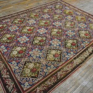Blue and brown low-pile rug with a repeating motif of colorful floral squares on hardwood flooring.