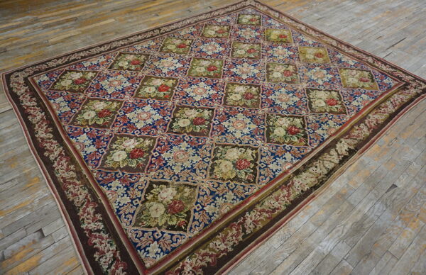 Blue and brown low-pile rug with a repeating motif of colorful floral squares on hardwood flooring.