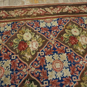 Intricate floral rug featuring red and cream roses within brown and blue medallions, lying on wood floorboards.