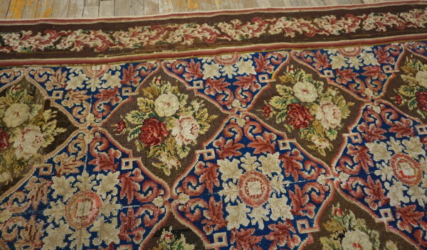 Intricate floral rug featuring red and cream roses within brown and blue medallions, lying on wood floorboards.