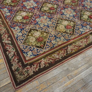 Intricate low-pile rug with blue and brown octagonal floral patterns rests on distressed light gray floorboards.