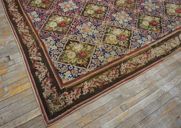 Intricate low-pile rug with blue and brown octagonal floral patterns rests on distressed light gray floorboards.