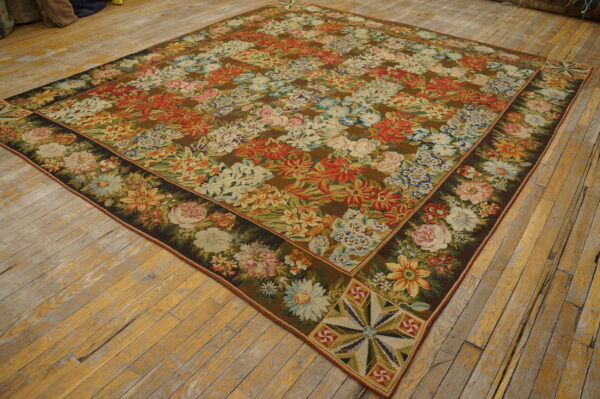 Square brown rug featuring dense repeating multicolor floral patterns and dark borders rests on distressed wood flooring.