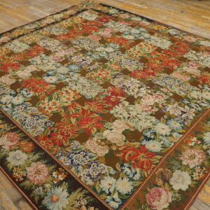 Multicolored floral rug with dense red, white, and pink bouquets on a dark brown ground over light wood planks.