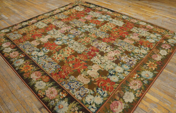 Multicolored floral rug with dense red, white, and pink bouquets on a dark brown ground over light wood planks.