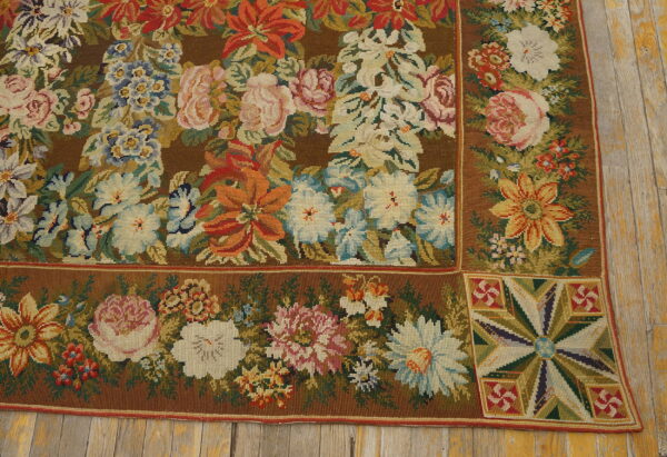 Brown low-pile rug with a detailed border and multicolor floral pattern resting on distressed yellow wood planks.
