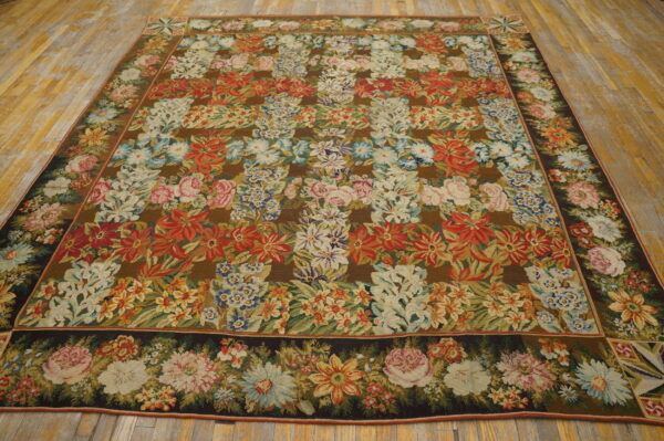 Multicolored floral tapestry rug with a brown field and dark border, displayed on distressed wood flooring.