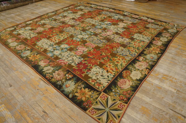 Flatweave rug with a dense multi-colored floral pattern and ornate border on distressed light wood flooring.