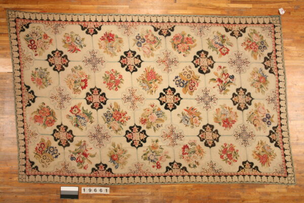 Low-pile rug with colorful floral bouquets and black geometric medallions on a cream field over wood floor.