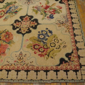 Low-pile cream rug with colorful floral panels and a black and red geometric border on wood flooring.