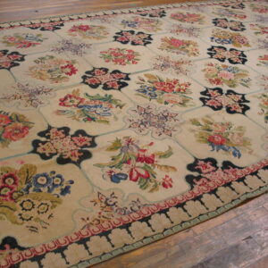 Multicolor floral rug with a pale background and black geometric grid border rests on hardwood planks.