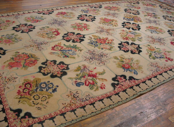 Multicolor floral rug with a pale background and black geometric grid border rests on hardwood planks.