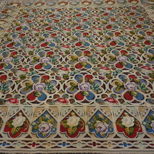 Low-pile rug with a beige background, vibrant red and blue floral medallions, and a decorative border on wood planks.