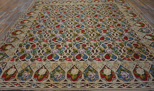 Low-pile rug with a beige background, vibrant red and blue floral medallions, and a decorative border on wood planks.